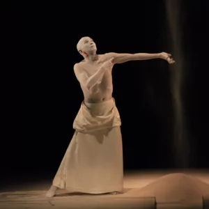 Danseur de butô de la compagnie Sankai Juku, le corps recouvert de blanc, dans une posture lente et expressive sur scène.