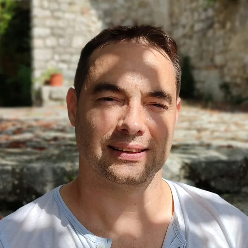 Portrait de Mickaël Chalopin, art-thérapeute et professeur de danse, souriant en extérieur devant un mur de pierre